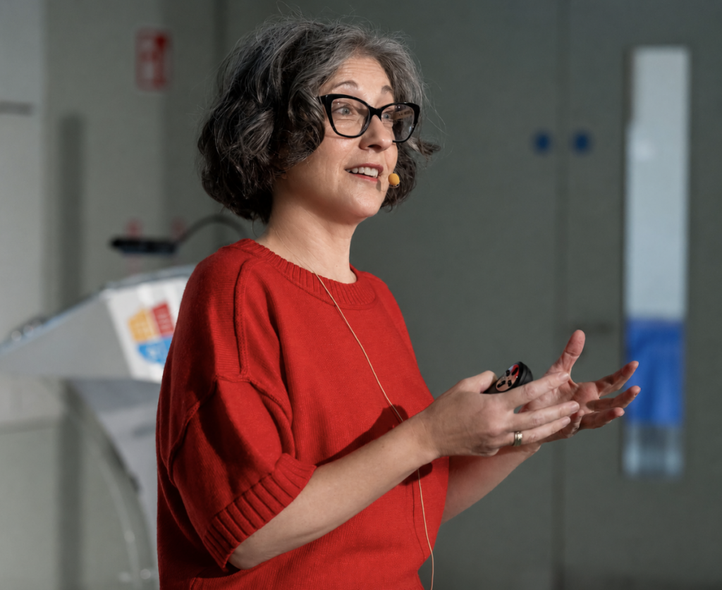 photo of woman (Robin DeRosa) with brownish gray hair and black glasses, wearing a red sweater and gesturing while speaking